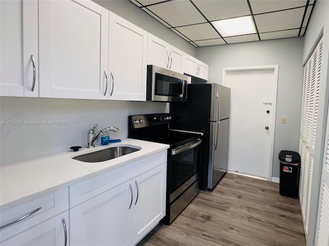 kitchen featuring sink, a paneled ceiling, light wood-type flooring, stainless steel appliances, and white cabinets