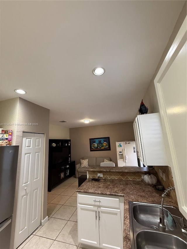 kitchen featuring sink, light tile patterned floors, stainless steel refrigerator, white cabinetry, and kitchen peninsula