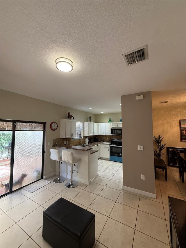 kitchen with a kitchen bar, light tile patterned floors, appliances with stainless steel finishes, kitchen peninsula, and white cabinets