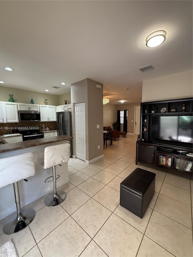 kitchen featuring a kitchen bar, white cabinetry, refrigerator, light tile patterned floors, and black / electric stove