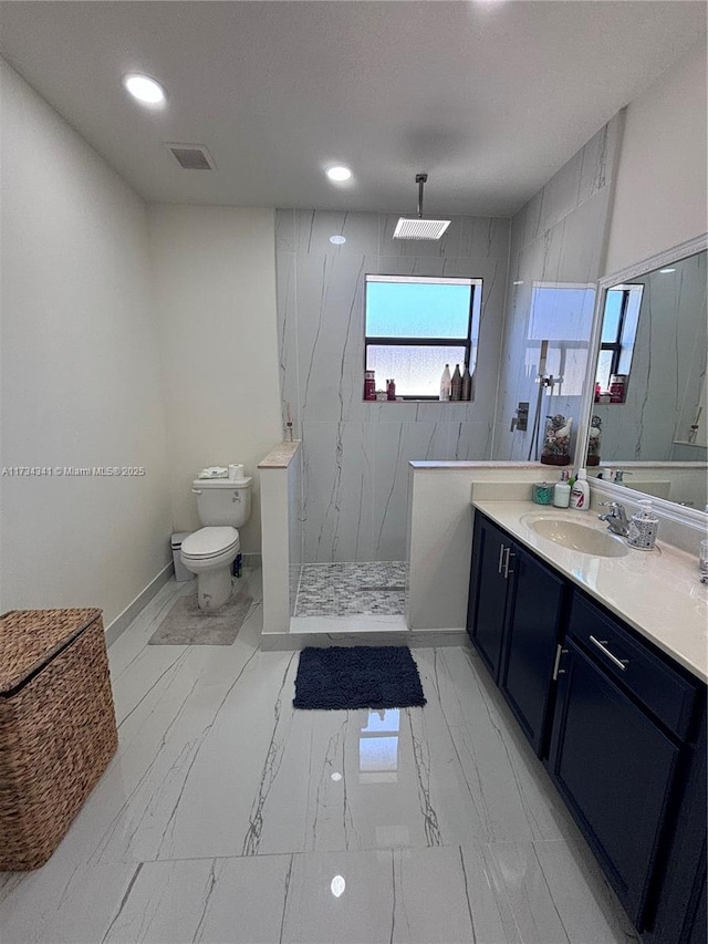 bathroom with tiled shower, vanity, and toilet