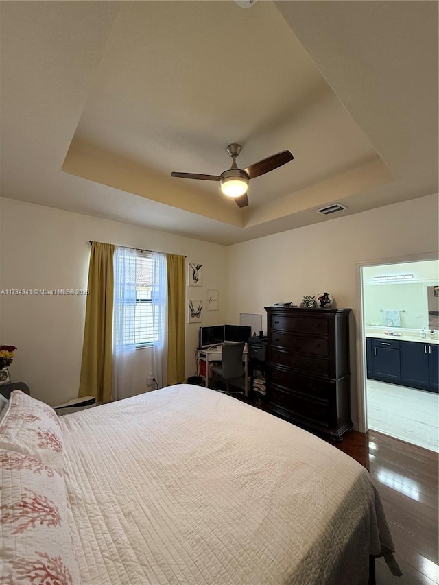 bedroom with dark wood-type flooring, connected bathroom, and a raised ceiling