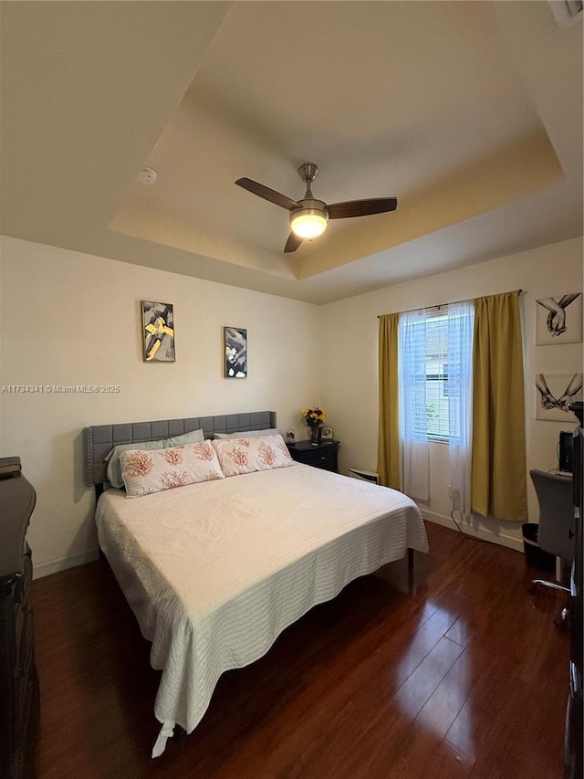 bedroom with dark hardwood / wood-style floors, a raised ceiling, and ceiling fan