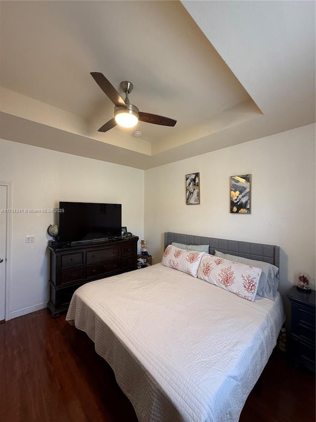 bedroom featuring dark wood-type flooring, a raised ceiling, and ceiling fan