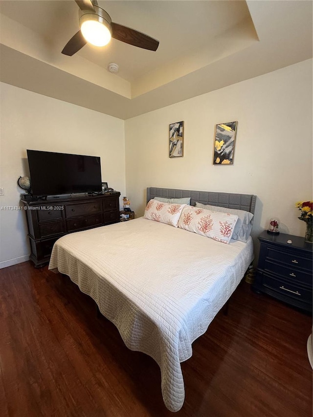 bedroom with a tray ceiling, dark wood-type flooring, and ceiling fan