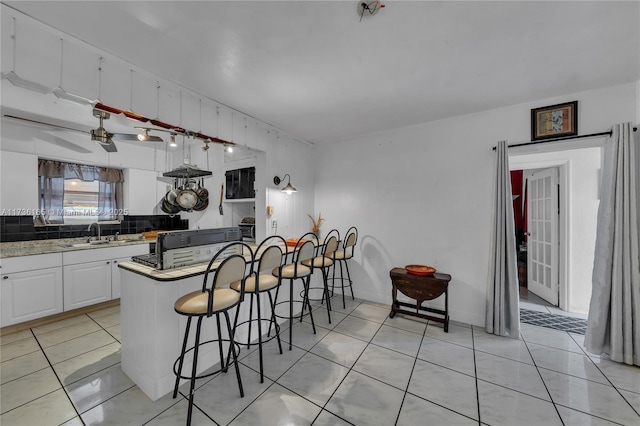 kitchen featuring light tile patterned floors, sink, a breakfast bar area, white cabinetry, and kitchen peninsula