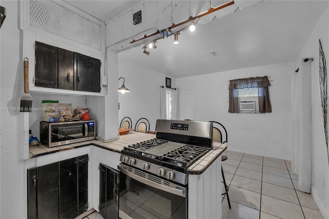 kitchen with appliances with stainless steel finishes, white cabinetry, light tile patterned floors, tile counters, and kitchen peninsula