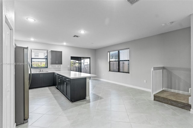 kitchen with sink, light tile patterned floors, stainless steel refrigerator, and kitchen peninsula