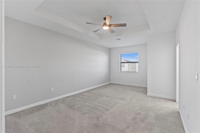 empty room featuring a raised ceiling, light carpet, and ceiling fan