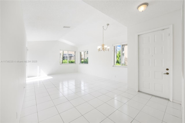 tiled spare room featuring vaulted ceiling, a wealth of natural light, a notable chandelier, and a textured ceiling