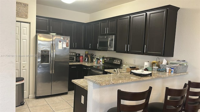 kitchen featuring light stone counters, a kitchen bar, kitchen peninsula, and appliances with stainless steel finishes