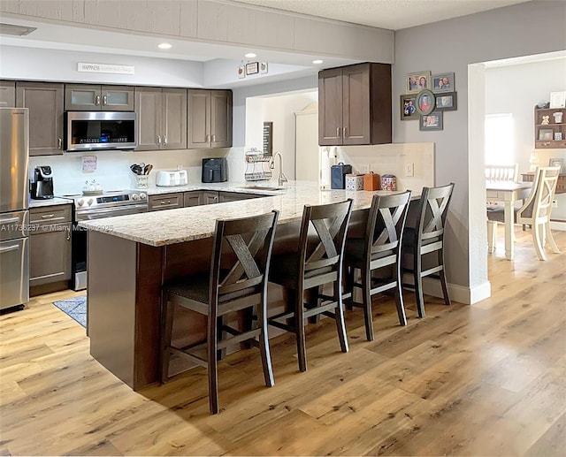 kitchen with light stone counters, stainless steel appliances, a kitchen bar, and kitchen peninsula