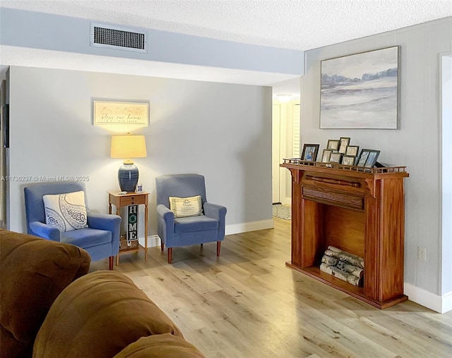 sitting room featuring visible vents, baseboards, a textured ceiling, and light wood finished floors