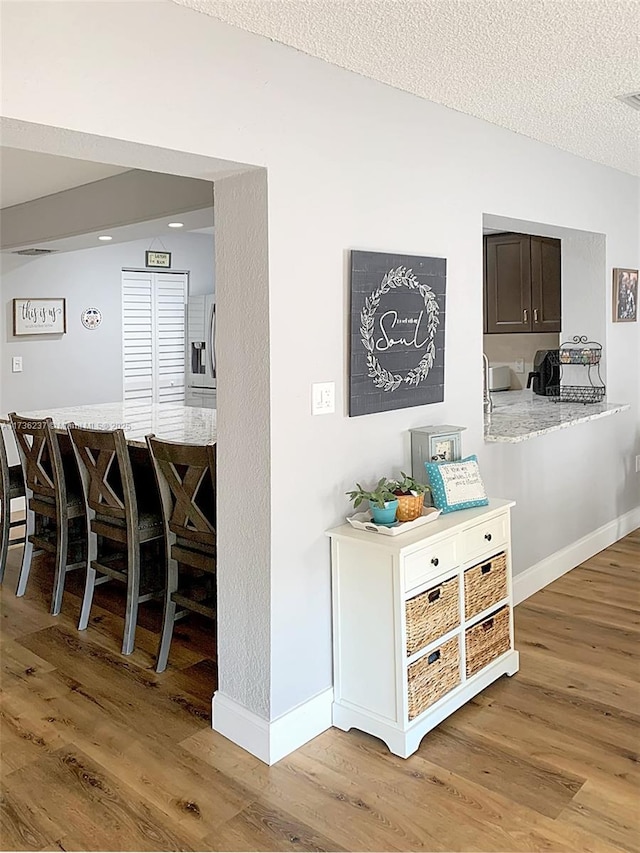 hallway featuring baseboards, a textured ceiling, vaulted ceiling, and light wood finished floors