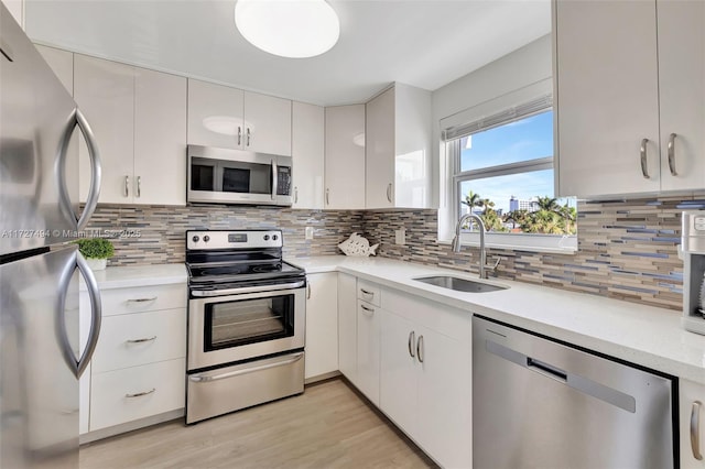 kitchen featuring stainless steel appliances, a sink, white cabinets, light countertops, and decorative backsplash