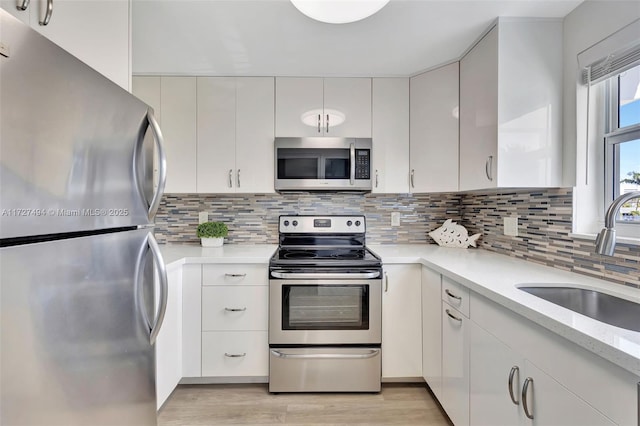 kitchen with tasteful backsplash, appliances with stainless steel finishes, light countertops, white cabinetry, and a sink