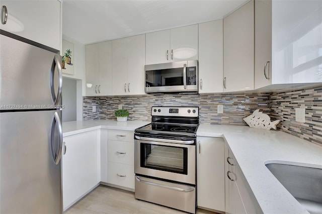 kitchen featuring stainless steel appliances, a sink, white cabinets, light stone countertops, and tasteful backsplash