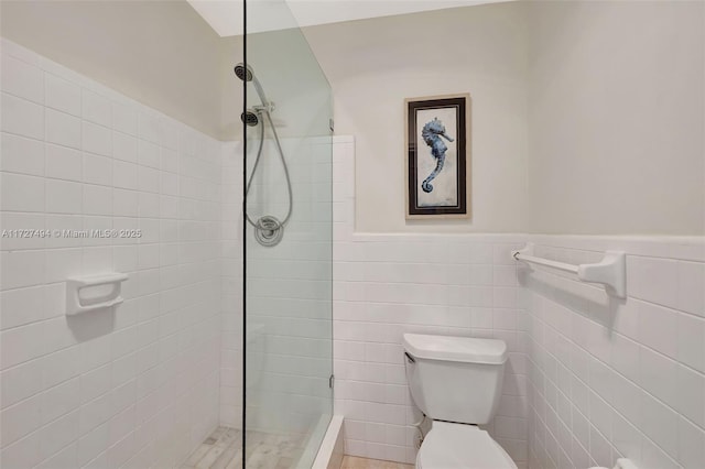 bathroom with a wainscoted wall, a tile shower, tile walls, and toilet