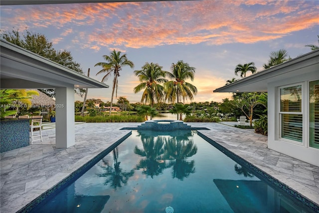 pool at dusk with a patio area and a pool with connected hot tub