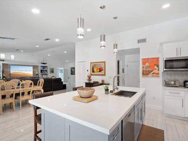 kitchen featuring an island with sink, sink, white cabinets, hanging light fixtures, and stainless steel appliances