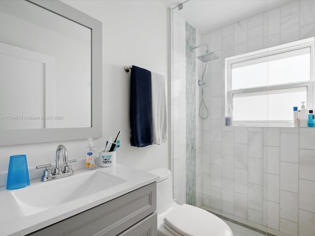 bathroom with tiled shower, vanity, and toilet