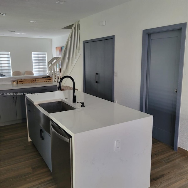 kitchen featuring dark wood-type flooring, stainless steel dishwasher, and an island with sink