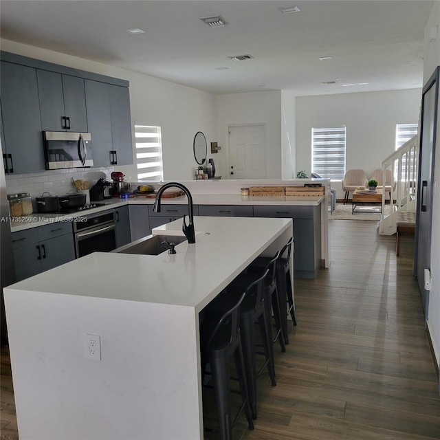 kitchen featuring an island with sink, sink, a kitchen breakfast bar, stainless steel appliances, and plenty of natural light