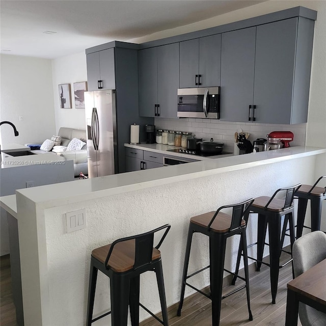 kitchen featuring appliances with stainless steel finishes, kitchen peninsula, a breakfast bar area, and gray cabinetry