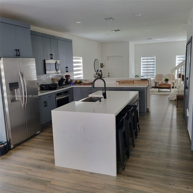 kitchen with wood-type flooring, sink, a kitchen breakfast bar, a kitchen island with sink, and stainless steel appliances