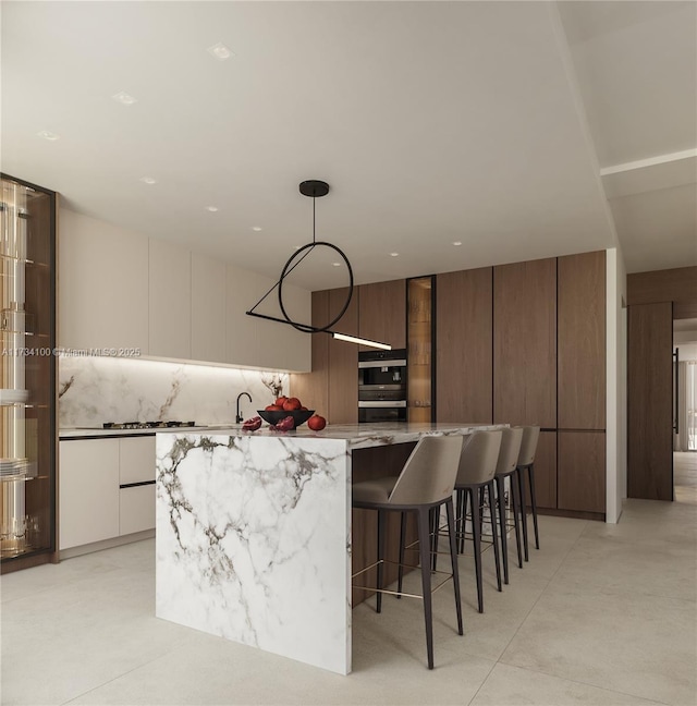 kitchen featuring decorative light fixtures, white cabinets, backsplash, a center island, and light stone counters