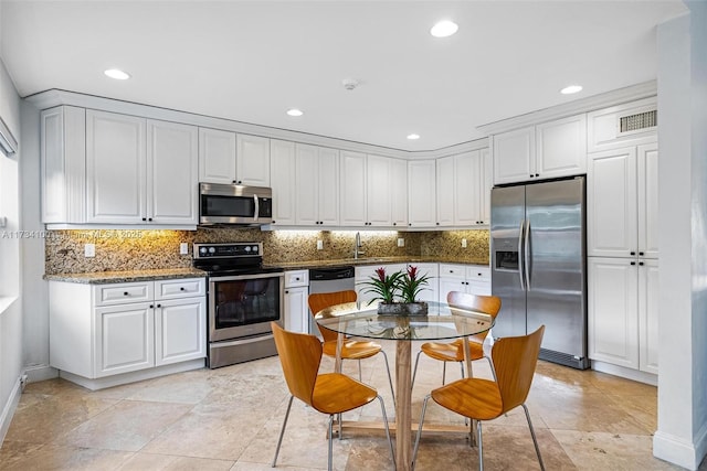 kitchen with tasteful backsplash, white cabinets, appliances with stainless steel finishes, and dark stone counters