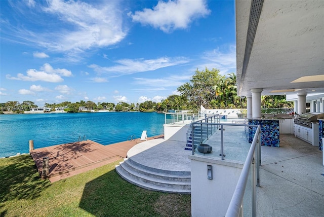 view of swimming pool featuring a water view, an outdoor kitchen, a bar, and area for grilling