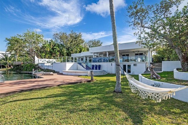 rear view of property featuring a deck with water view and a lawn