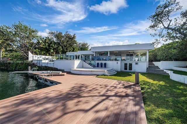 back of property with a water view, a dock, and a lawn