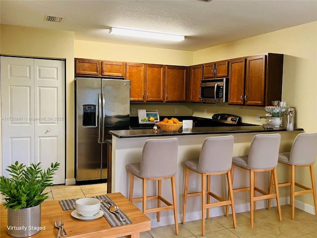 kitchen with a peninsula, dark countertops, a breakfast bar, and stainless steel appliances