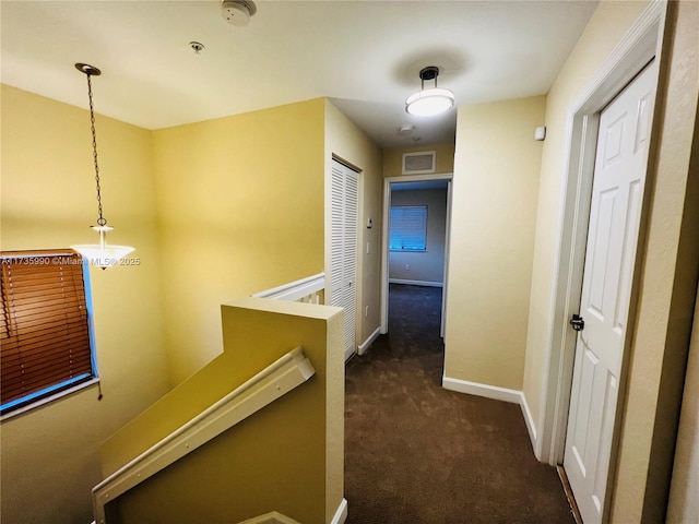 hallway with baseboards, an upstairs landing, dark carpet, and visible vents