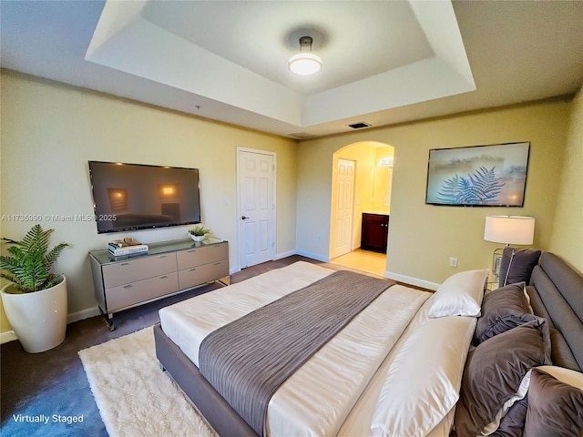 carpeted bedroom featuring ensuite bathroom and a raised ceiling