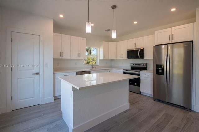 kitchen featuring wood-type flooring, a kitchen island, pendant lighting, stainless steel appliances, and white cabinets