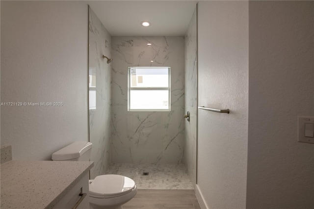 bathroom featuring vanity, wood-type flooring, tiled shower, and toilet