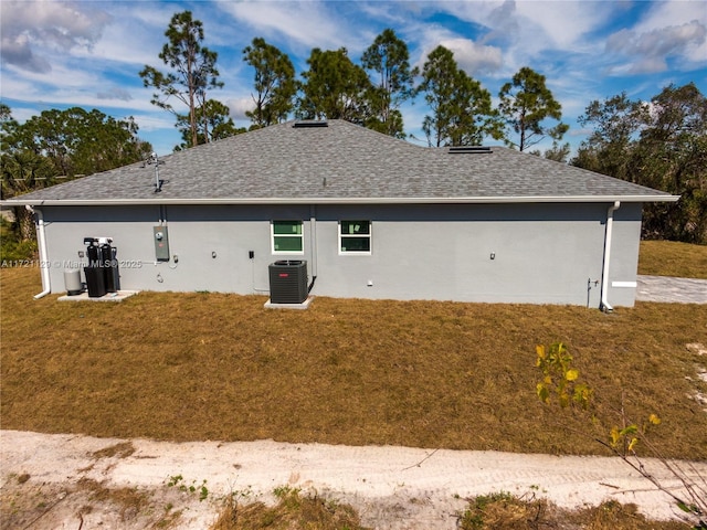 rear view of property featuring central AC and a lawn