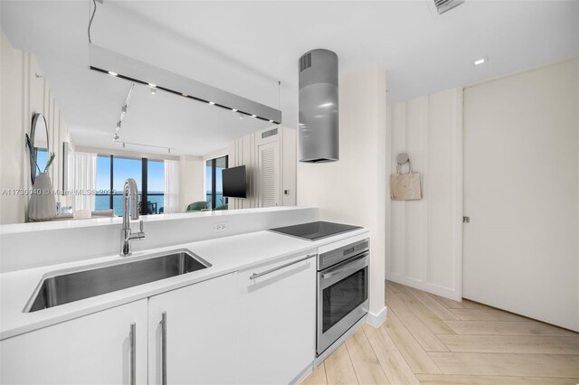 2201 Collins Ave Unit 1128, Miami Beach, FL 33139 - kitchen with stainless steel oven, black electric cooktop, range hood, a sink, and track lighting