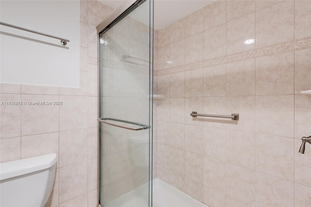 bathroom featuring tile walls, a shower with door, and toilet