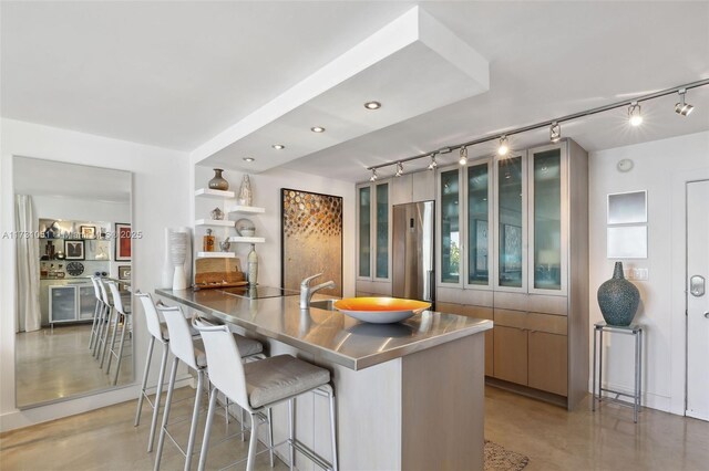 kitchen featuring stainless steel refrigerator, sink, a kitchen breakfast bar, stainless steel counters, and track lighting