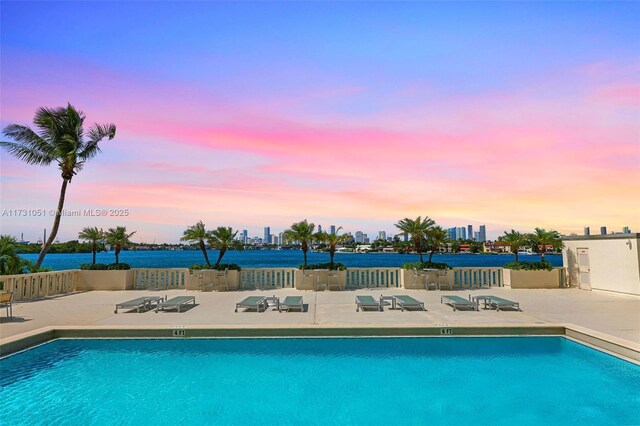 pool at dusk featuring a patio and a water view