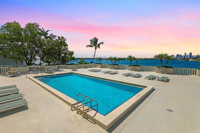 pool at dusk featuring a patio area and a water view