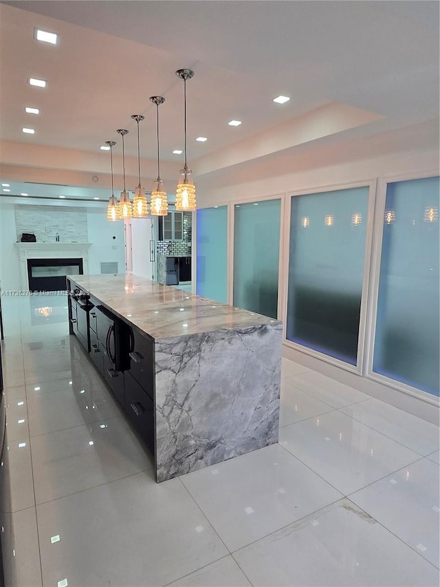 kitchen featuring light tile patterned flooring, a large island, light stone countertops, and hanging light fixtures