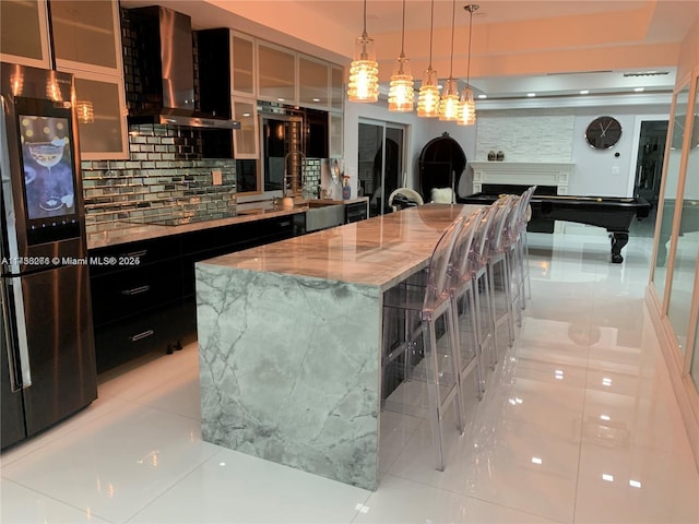 kitchen featuring a spacious island, stainless steel fridge, a breakfast bar, and wall chimney exhaust hood