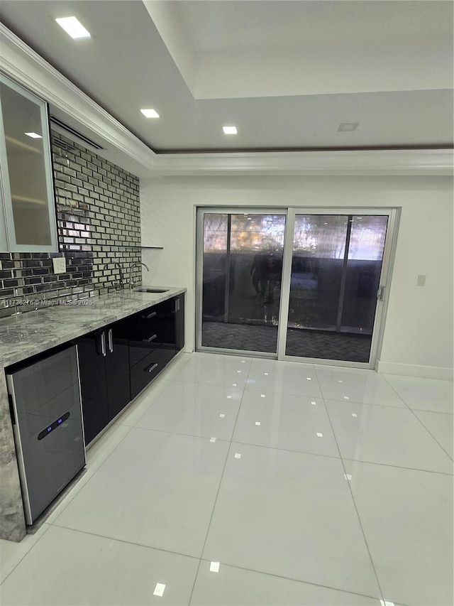 kitchen with light tile patterned flooring, sink, light stone counters, tasteful backsplash, and a tray ceiling