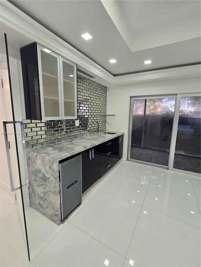 kitchen featuring sink, tasteful backsplash, light tile patterned floors, a tray ceiling, and light stone countertops