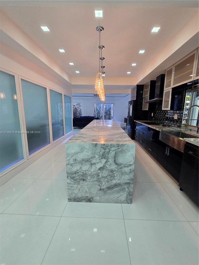 kitchen featuring pendant lighting, light tile patterned floors, backsplash, and wall chimney exhaust hood